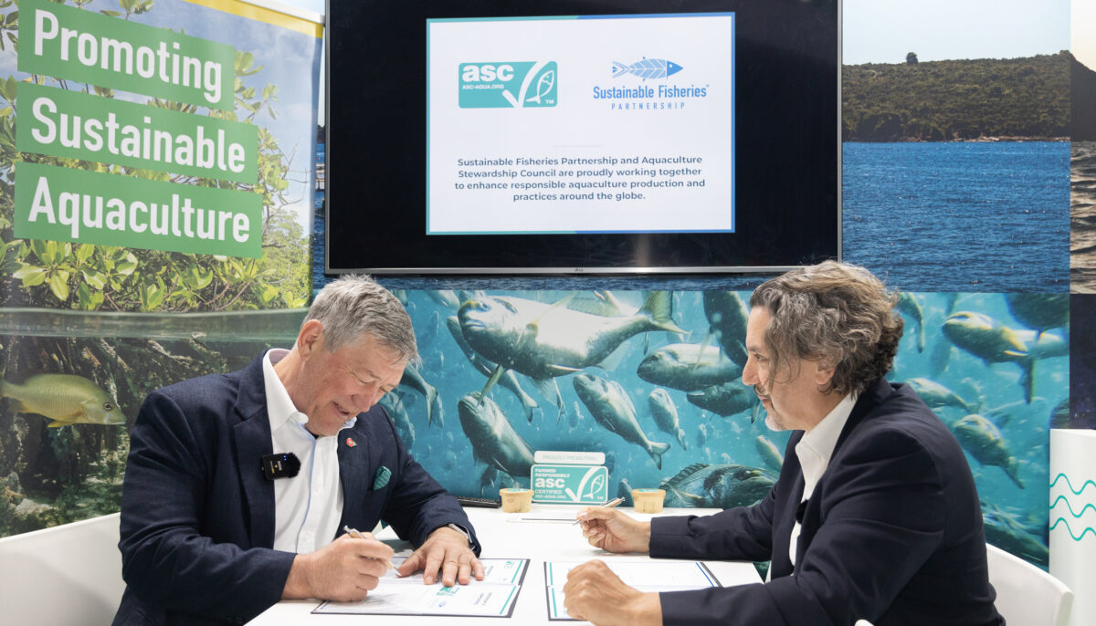 Chris y Jim sentados firmando un memorándum de acuerdo en la Seafood Expo Global.