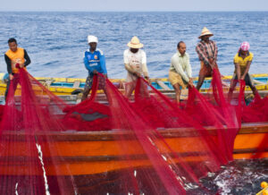 Group of fishers hauling in a red net on a small fishing boat