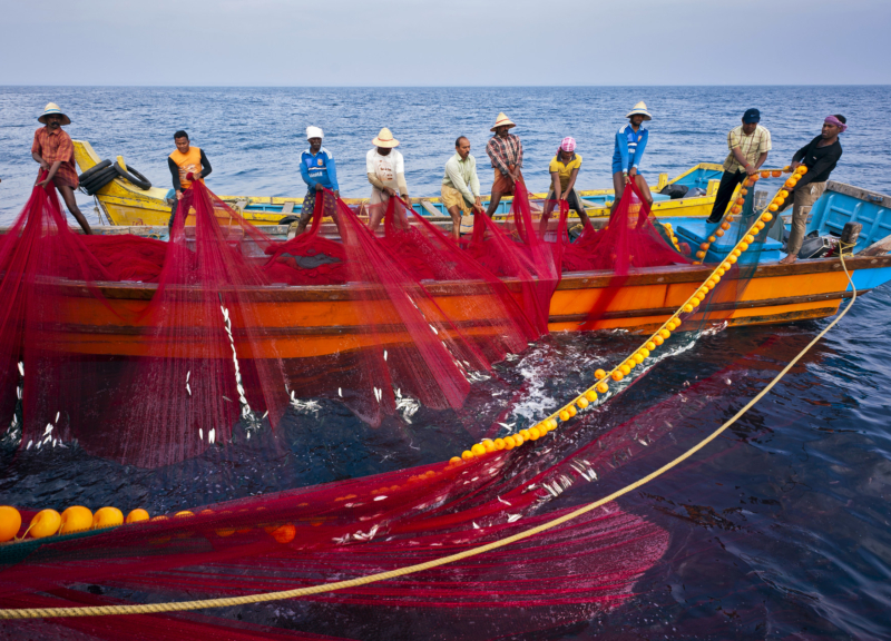 Grupo de pescadores recogiendo una red roja en un pequeño barco pesquero