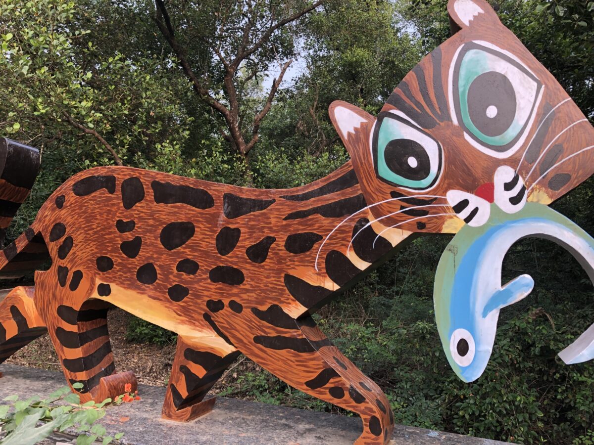 Metal sculpture of Macha the Fishing Cat, showing a cartoon fishing cat holding a blue and white fish in its mouth