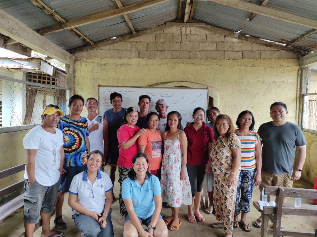 Members of Bluer Seas Philippines and SFP posed in front of a white board in an open-air classroom with members of a local fishing community