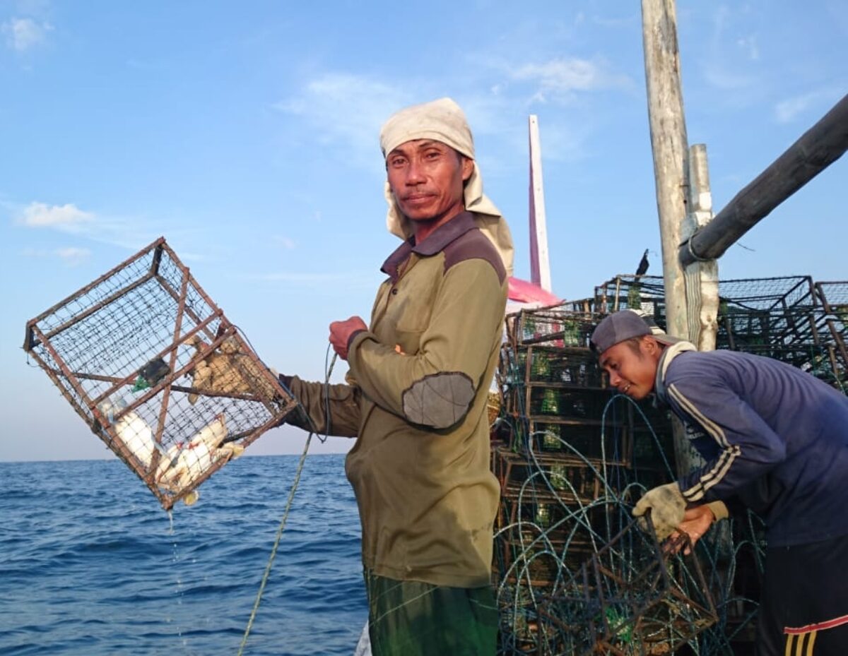 A blue swimming crab fisher holding a crab trap over the water