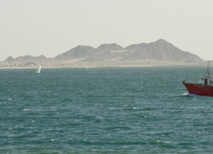 A red-hulled shrimping boat on the Sea of Cortez, with a mountainous coastline in the misty background