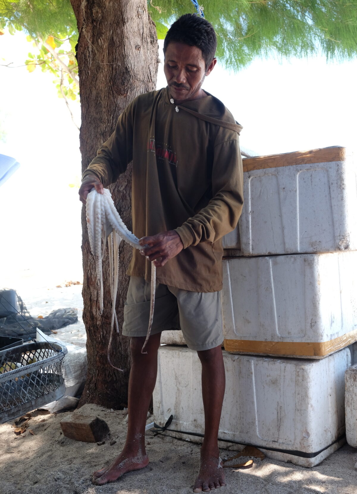 A man holding a freshly caught octopus, standing in front of a stack of white cooler boxes