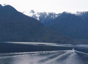 a solitary fishing boat heading out to sea with snow-covered mountains in the background