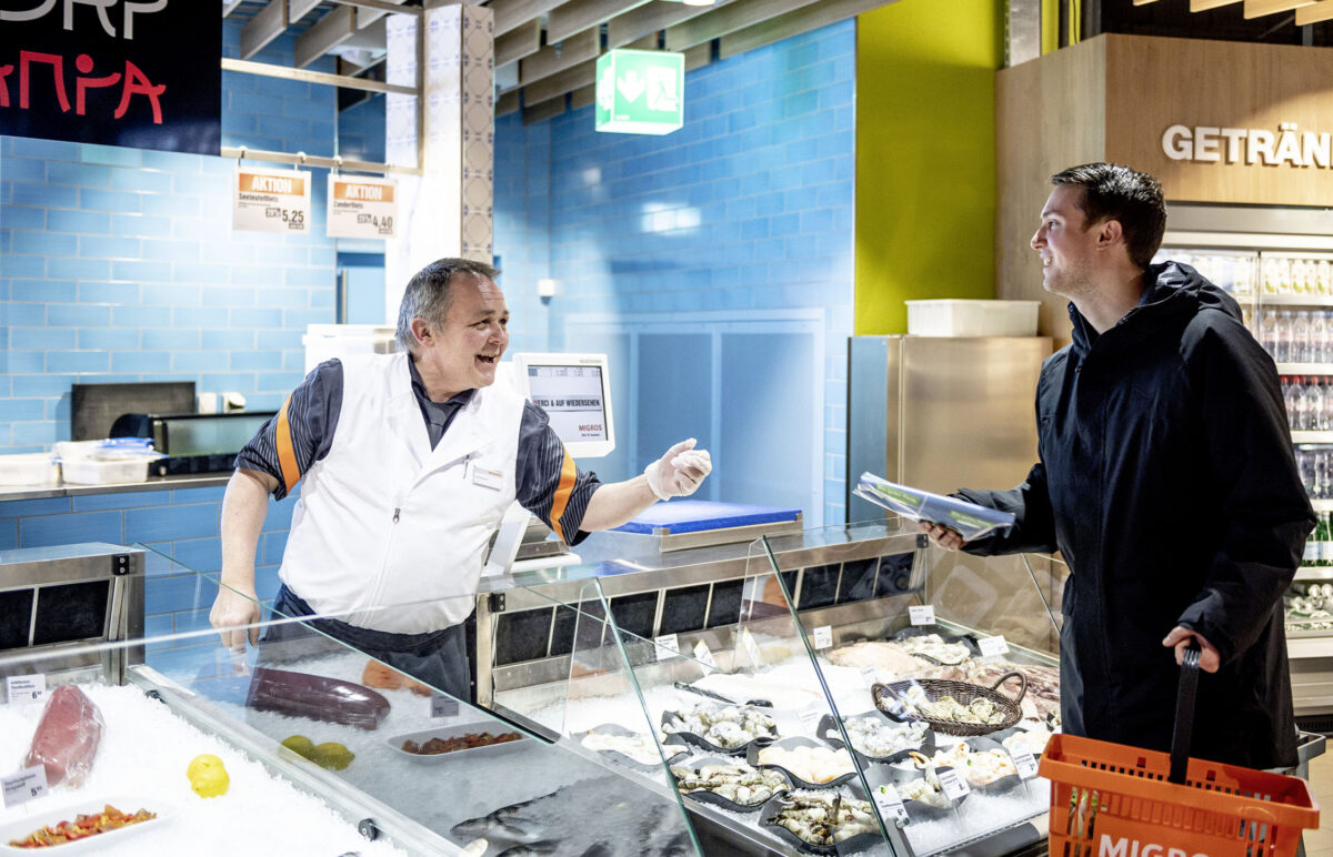 An employee serves a customer at the fish counter in a Migros supermarket.