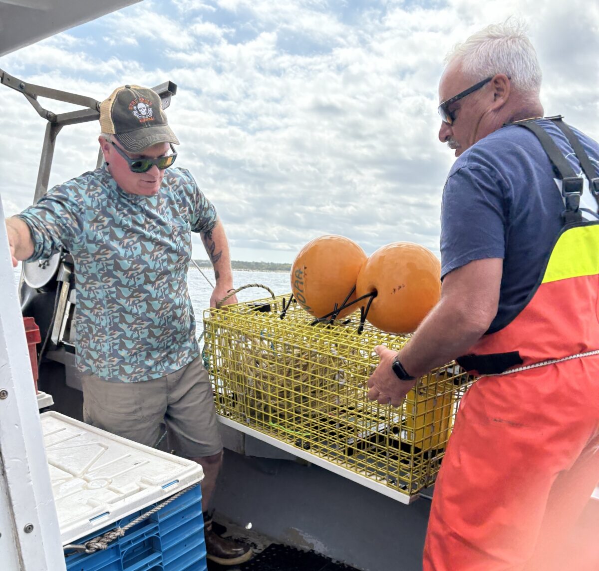 Two fishermen hauling a yellow metal on-demand trap with two orange buoy on top onto a lobster boat
