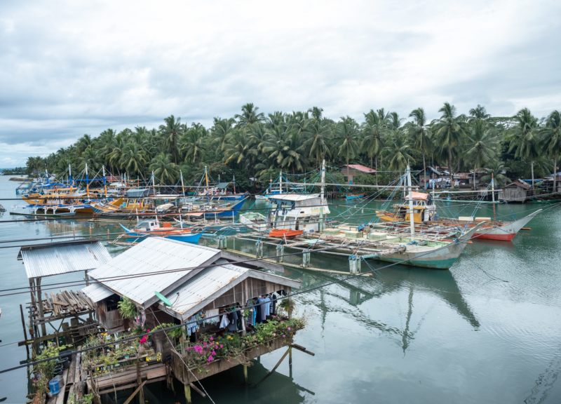 A fishing village in the Philippines, with multiple boats at the dock and small houses on stilts