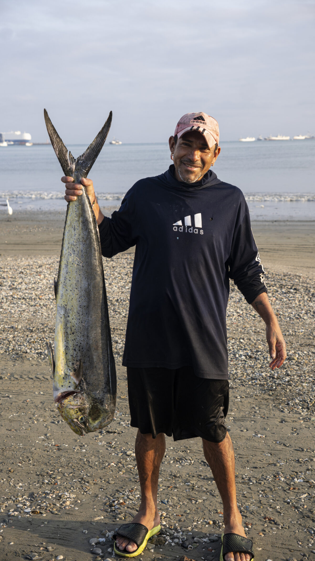 A fisherman standing on the beach holding a large mahi by the tail