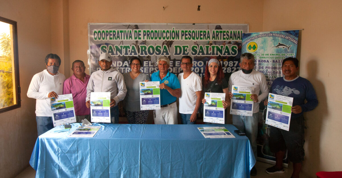 A group of people standing behind a table holding up signs about the mahi work