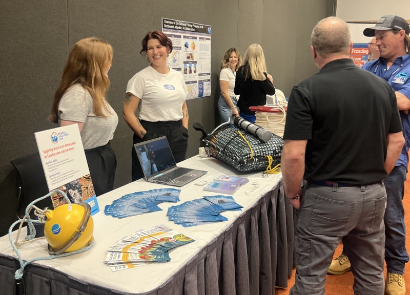 Bycatch Solutions Showcase 2025 - multiple people behind and in front of a table, with technology and yellow smart buoys on the table