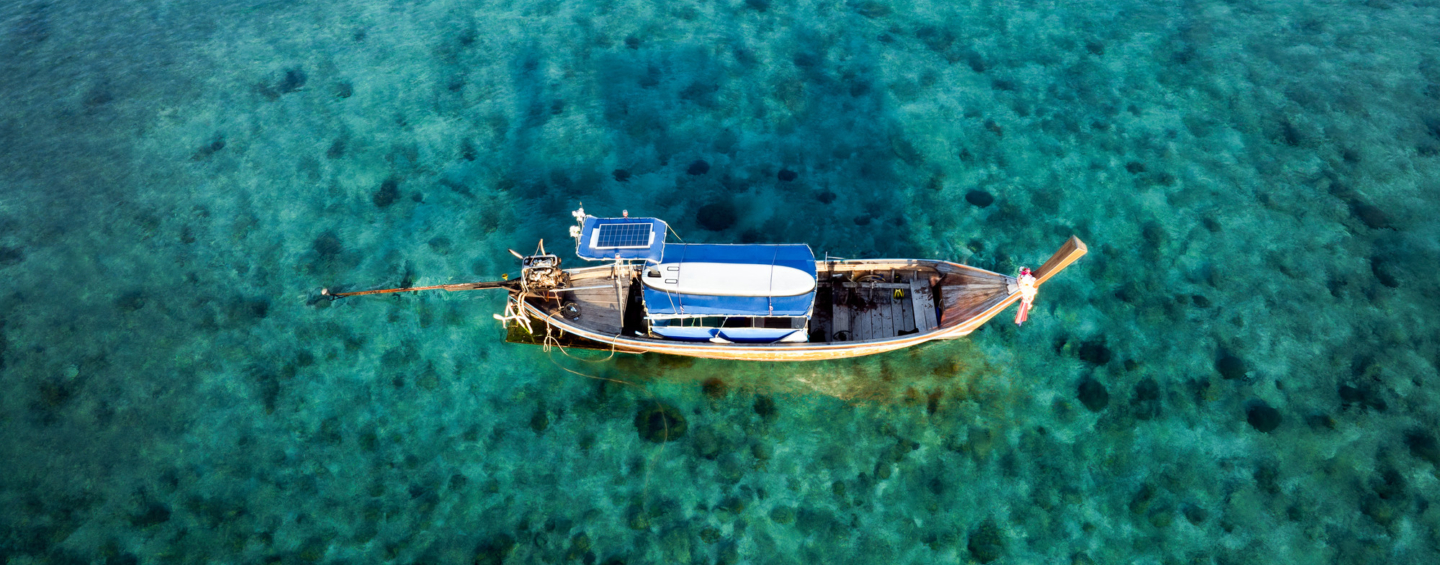 Drone shot of a traditional Thai longtail boat floating on clear turquoise waters in Thailand.