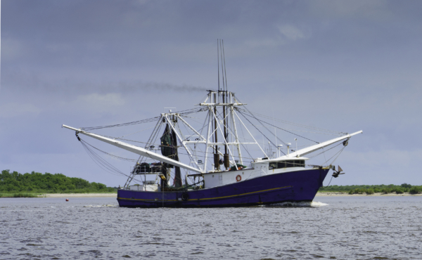 A shrimp boat passes the historic Sabine Pass Lighthouse