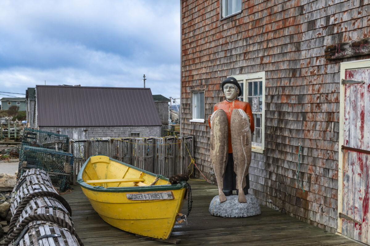 Statue of a fisherman holding two cod fish and an old fishing boat known as a dory in the fishing village of Peggy's Cove, in Southern Nova Scotia, Canada.
