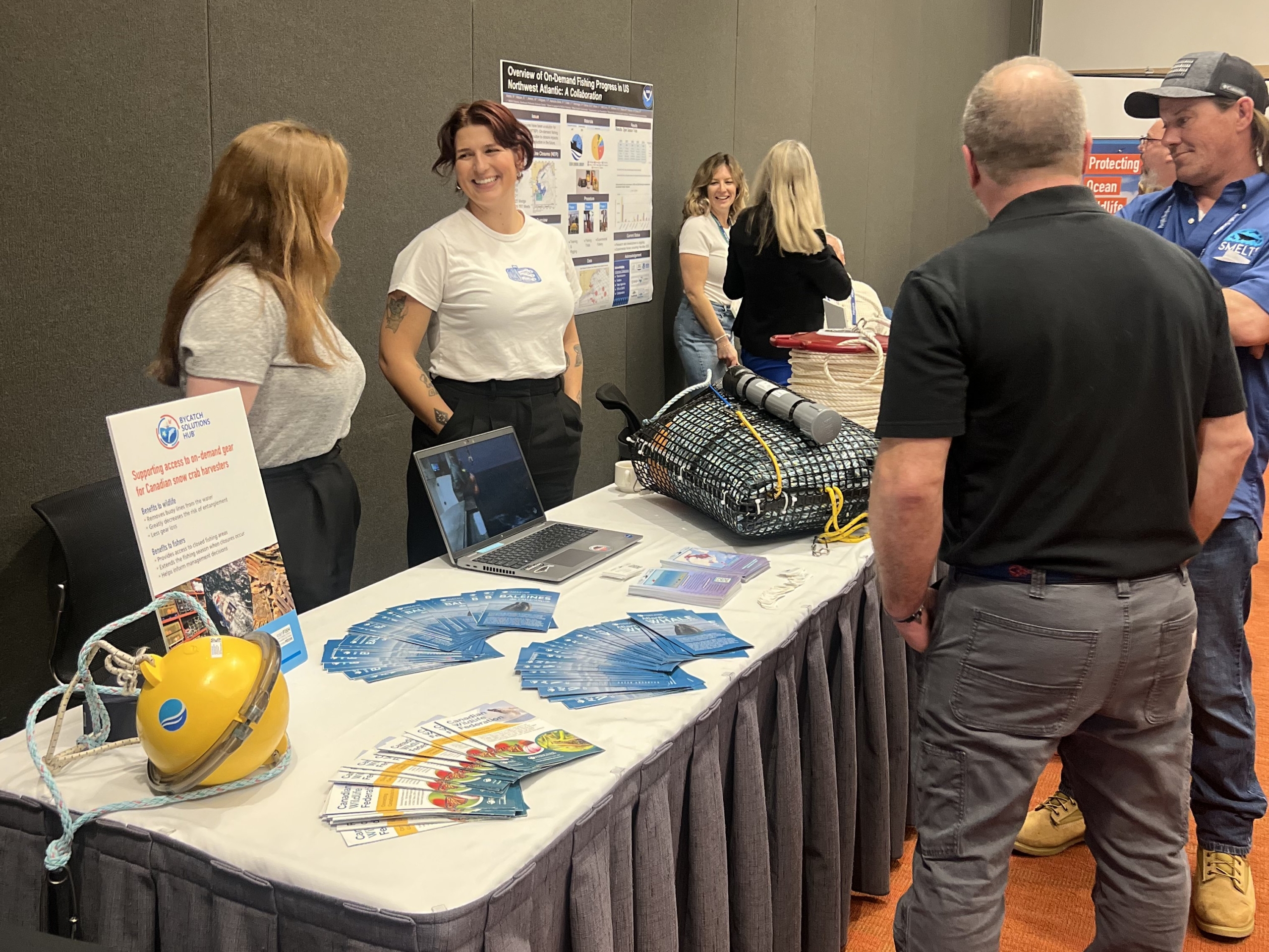 Bycatch Solutions Showcase 2025 - multiple people behind and in front of a table, with technology and yellow smart buoys on the table