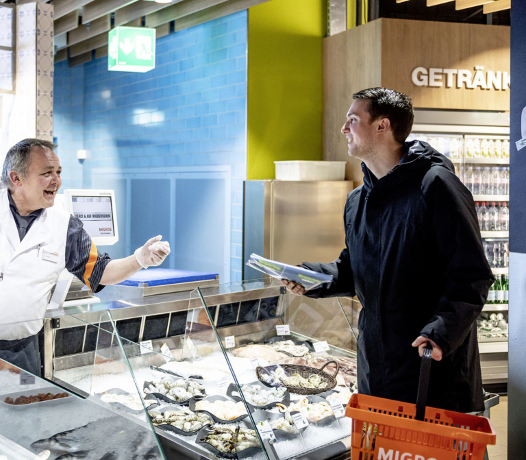 An employee serves a customer at the fish counter in a Migros supermarket.