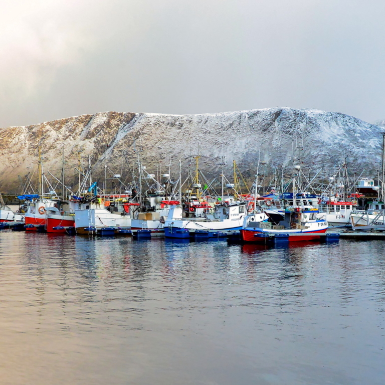 Norwegian fishing boats in harbor with snow-covered mountains behind them